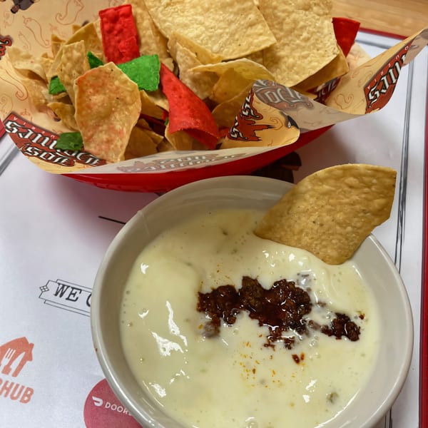 A bowl of queso with chorizo and a basket of tortilla chips, including red and green chips.