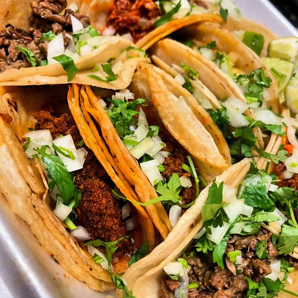 Close-up of Los Homies Taqueria's assorted tacos with meat, onions, cilantro, and lime wedges.