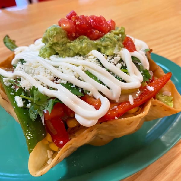 A vibrant Los Homies Taqueria taco salad in a crispy shell, topped with guacamole, tomatoes, and sour cream.