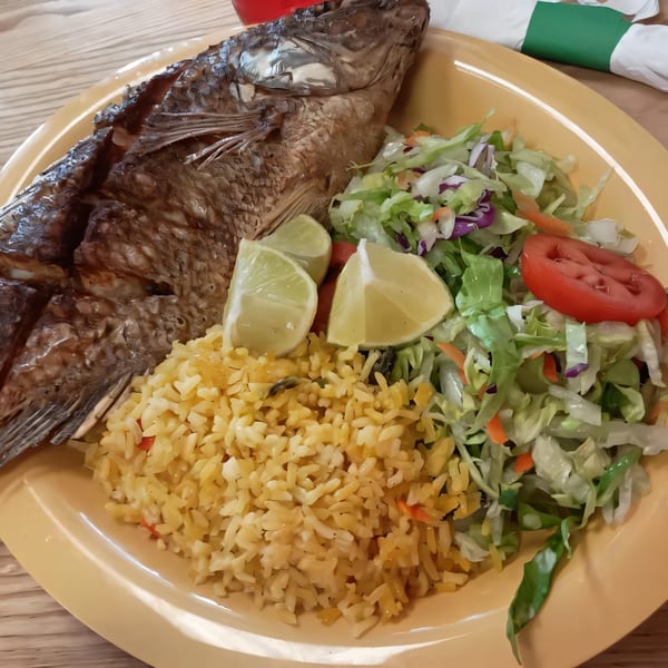 Whole fried fish with rice, salad, and lime wedges on a yellow plate at Los Homies Taqueria.