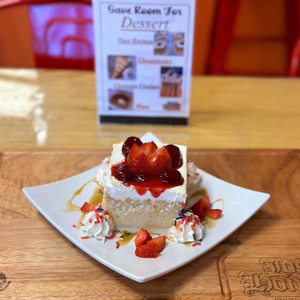 A slice of Tres Leches cake with whipped cream, strawberries, and sprinkles on a white plate.